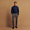 View 1 of product A man stands against a tan background, wearing the Turnbull & Asser Navy Wool Blend Weekend Fit Hayne Shirt tucked into gray dress pants with a black belt and shoes. He has short hair, a neutral expression, and his hands are in his pockets for a casual look.