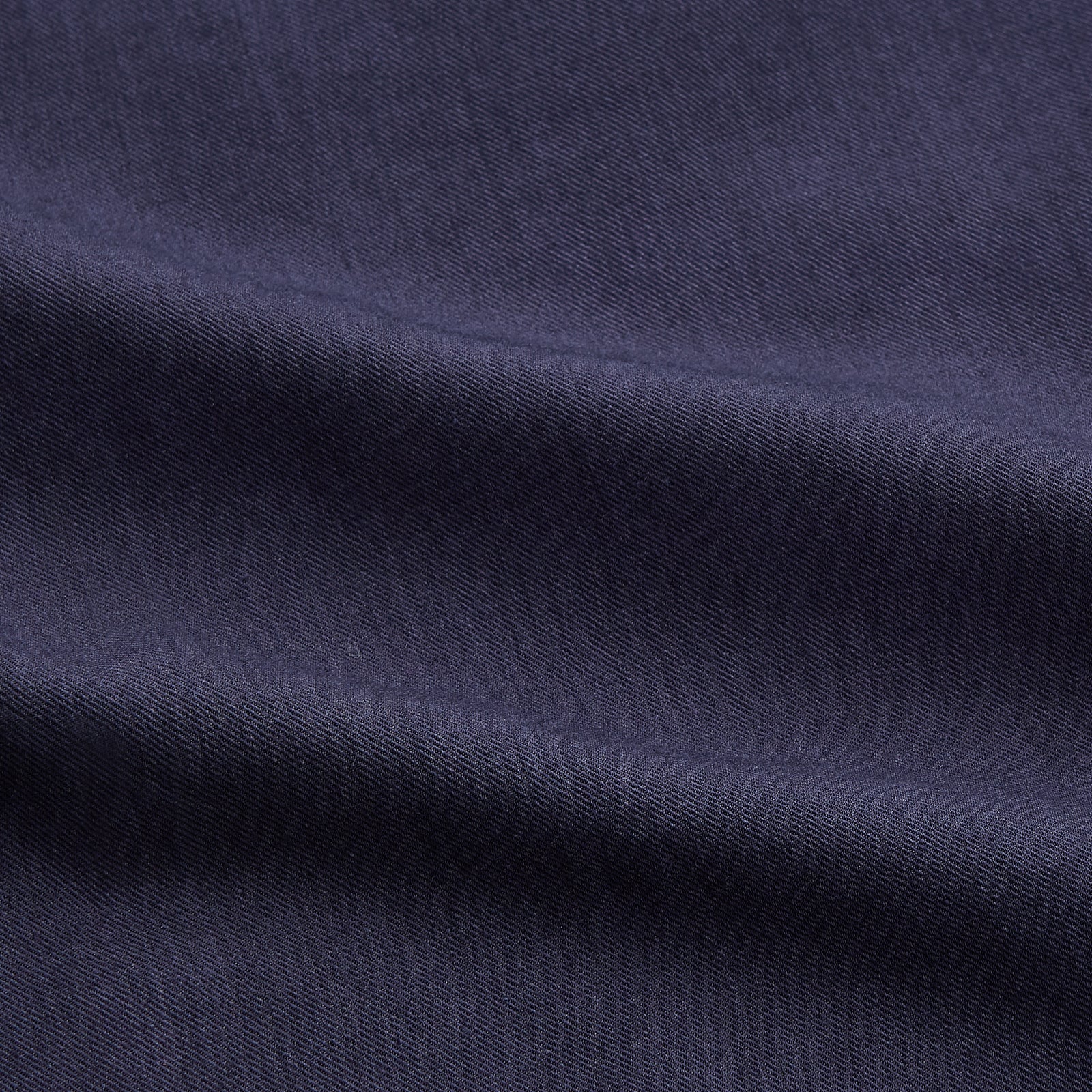 View 5 of product A man stands against a tan background, wearing the Turnbull & Asser Navy Wool Blend Weekend Fit Hayne Shirt tucked into gray dress pants with a black belt and shoes. He has short hair, a neutral expression, and his hands are in his pockets for a casual look.