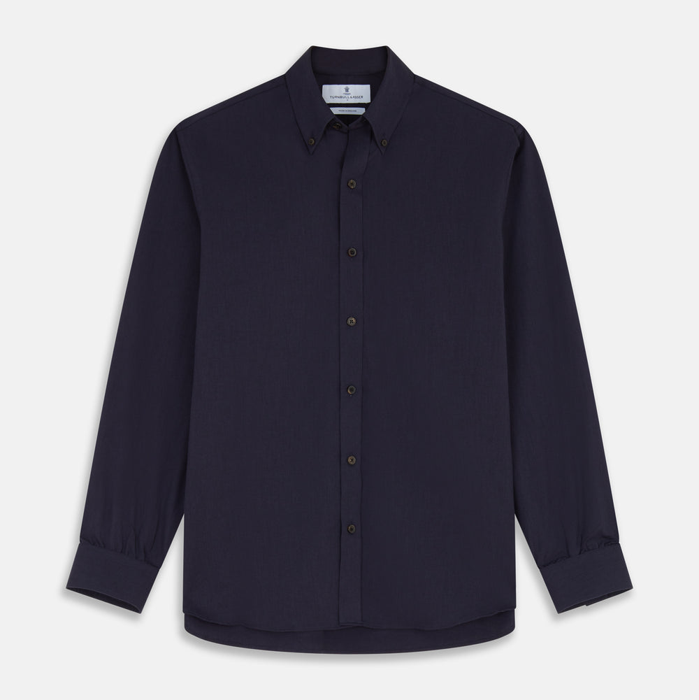 A man stands against a tan background, wearing the Turnbull & Asser Navy Wool Blend Weekend Fit Hayne Shirt tucked into gray dress pants with a black belt and shoes. He has short hair, a neutral expression, and his hands are in his pockets for a casual look.