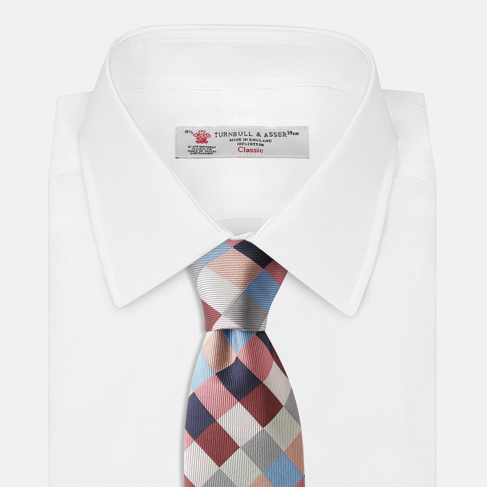 The Turnbull & Asser Pink and Blue Checkerboard Silk Tie is shown rolled up, highlighting its pink, blue, grey, and white pattern against a plain white background.