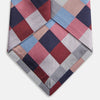 View 4 of product The Turnbull & Asser Pink and Blue Checkerboard Silk Tie is shown rolled up, highlighting its pink, blue, grey, and white pattern against a plain white background.