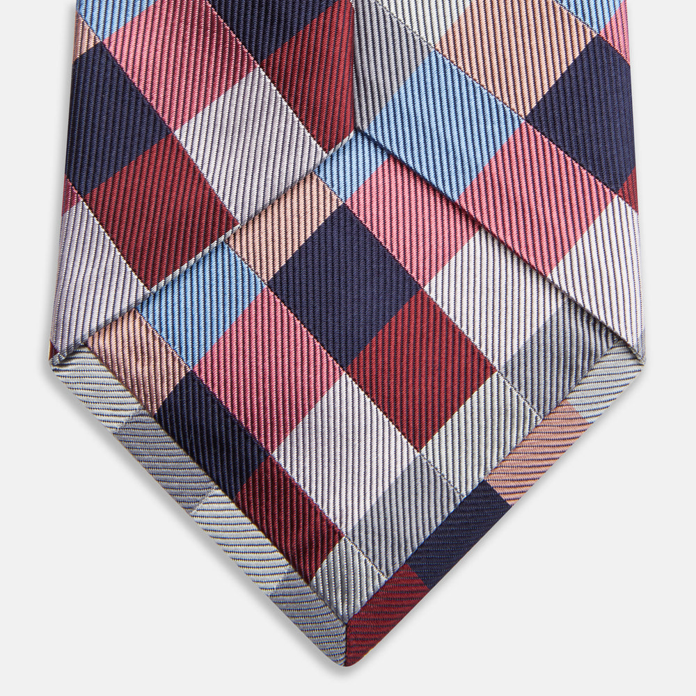 The Turnbull & Asser Pink and Blue Checkerboard Silk Tie is shown rolled up, highlighting its pink, blue, grey, and white pattern against a plain white background.