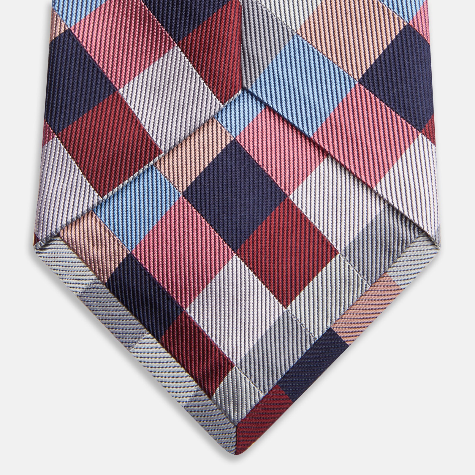 View 4 of product The Turnbull & Asser Pink and Blue Checkerboard Silk Tie is shown rolled up, highlighting its pink, blue, grey, and white pattern against a plain white background.