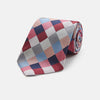View 1 of product The Turnbull & Asser Pink and Blue Checkerboard Silk Tie is shown rolled up, highlighting its pink, blue, grey, and white pattern against a plain white background.