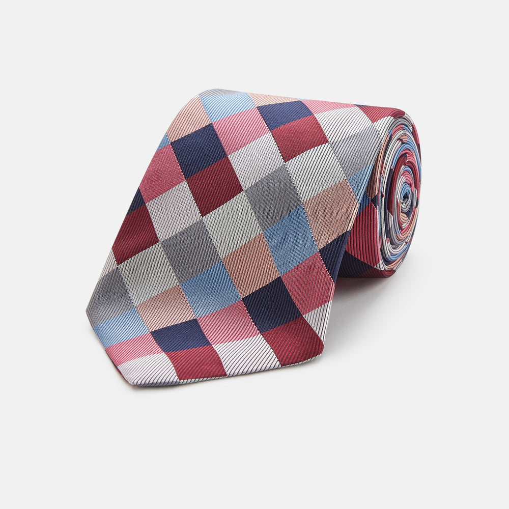 The Turnbull & Asser Pink and Blue Checkerboard Silk Tie is shown rolled up, highlighting its pink, blue, grey, and white pattern against a plain white background.