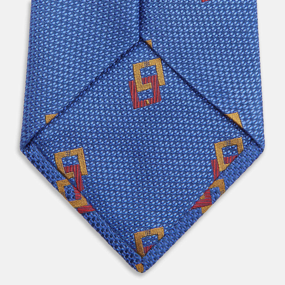The Blue Geometric Squares Silk Tie by Turnbull & Asser features a classic blue base with small yellow and red geometric shapes, making it a sophisticated textured silk accessory.