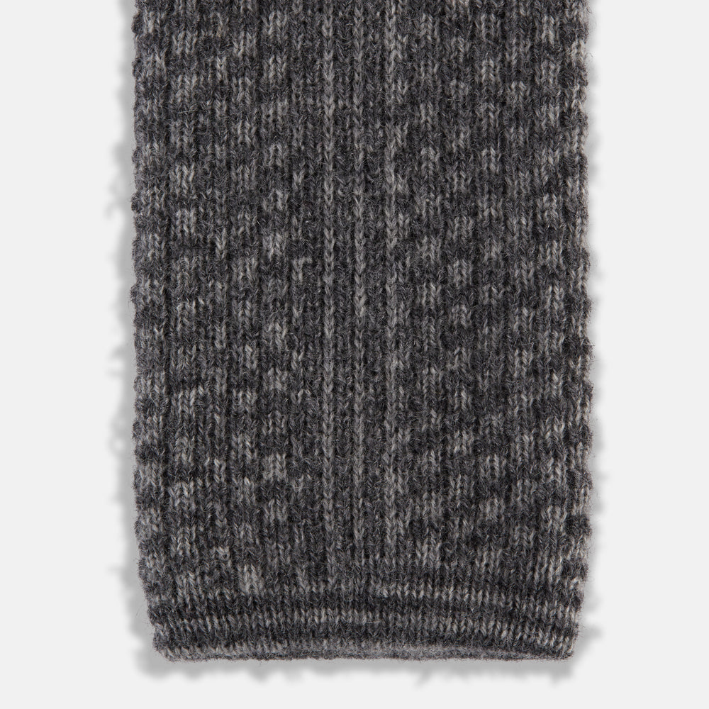 The Grey Multi Cashmere Knitted Tie by Turnbull & Asser features a textured checkered pattern, rolled and displayed on a white background—a refined menswear essential.
