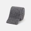 View 1 of product The Grey Multi Cashmere Knitted Tie by Turnbull & Asser features a textured checkered pattern, rolled and displayed on a white background—a refined menswear essential.