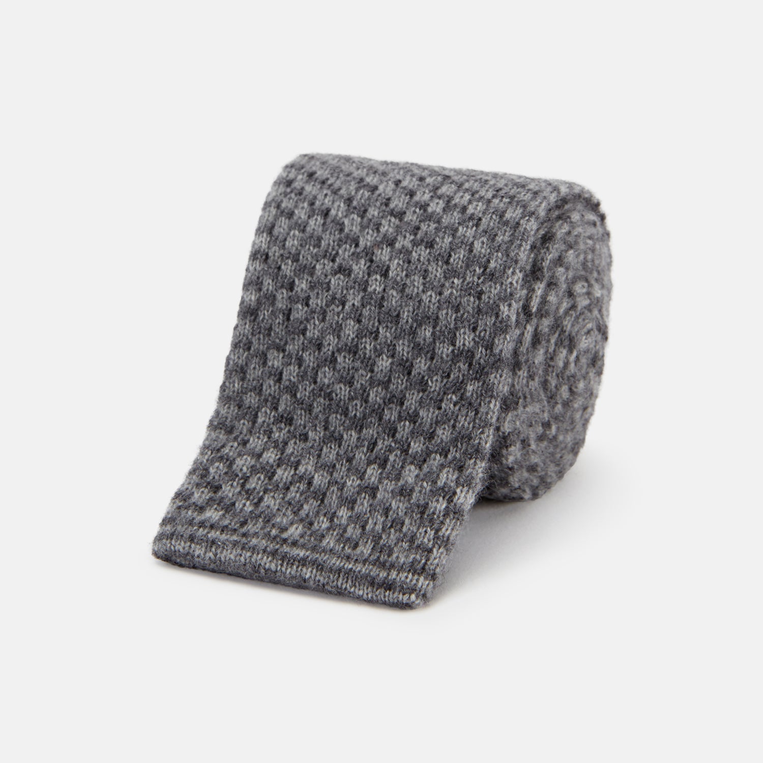 View 1 of product The Grey Multi Cashmere Knitted Tie by Turnbull & Asser features a textured checkered pattern, rolled and displayed on a white background—a refined menswear essential.