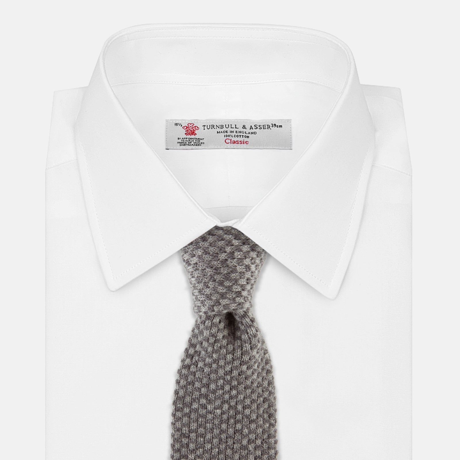 View 2 of product The Grey Multi Cashmere Knitted Tie by Turnbull & Asser features a textured checkered pattern, rolled and displayed on a white background—a refined menswear essential.