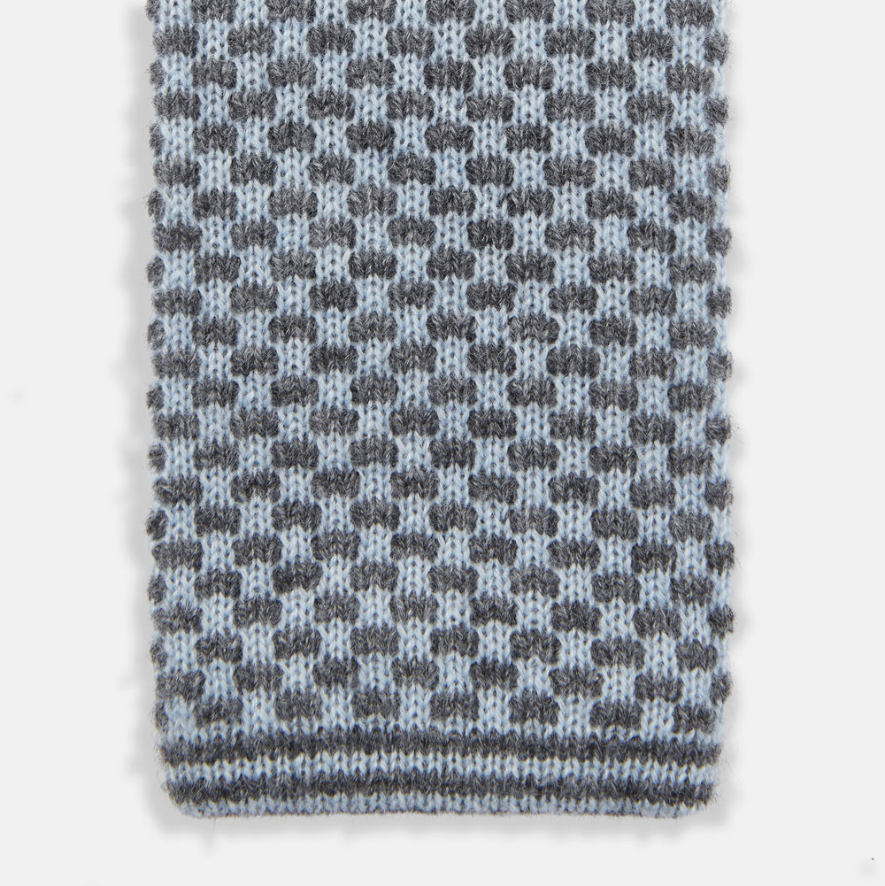 The Turnbull & Asser Pale Blue Multi Cashmere Knitted Tie features a subtle checkered pattern in black and light blue, making it a refined addition to your menswear collection. Shown rolled up on a plain white background.