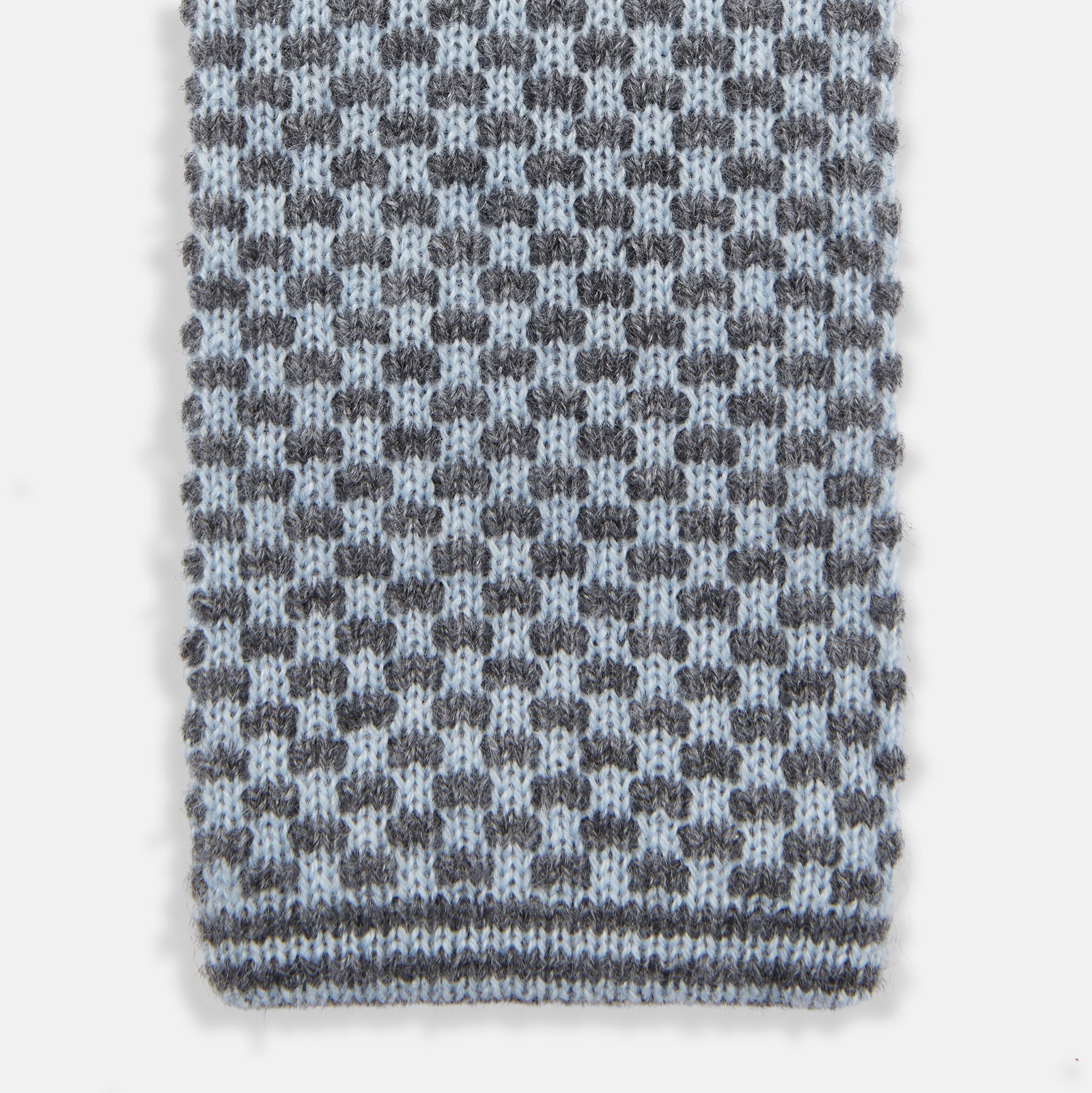View 2 of product The Turnbull & Asser Pale Blue Multi Cashmere Knitted Tie features a subtle checkered pattern in black and light blue, making it a refined addition to your menswear collection. Shown rolled up on a plain white background.