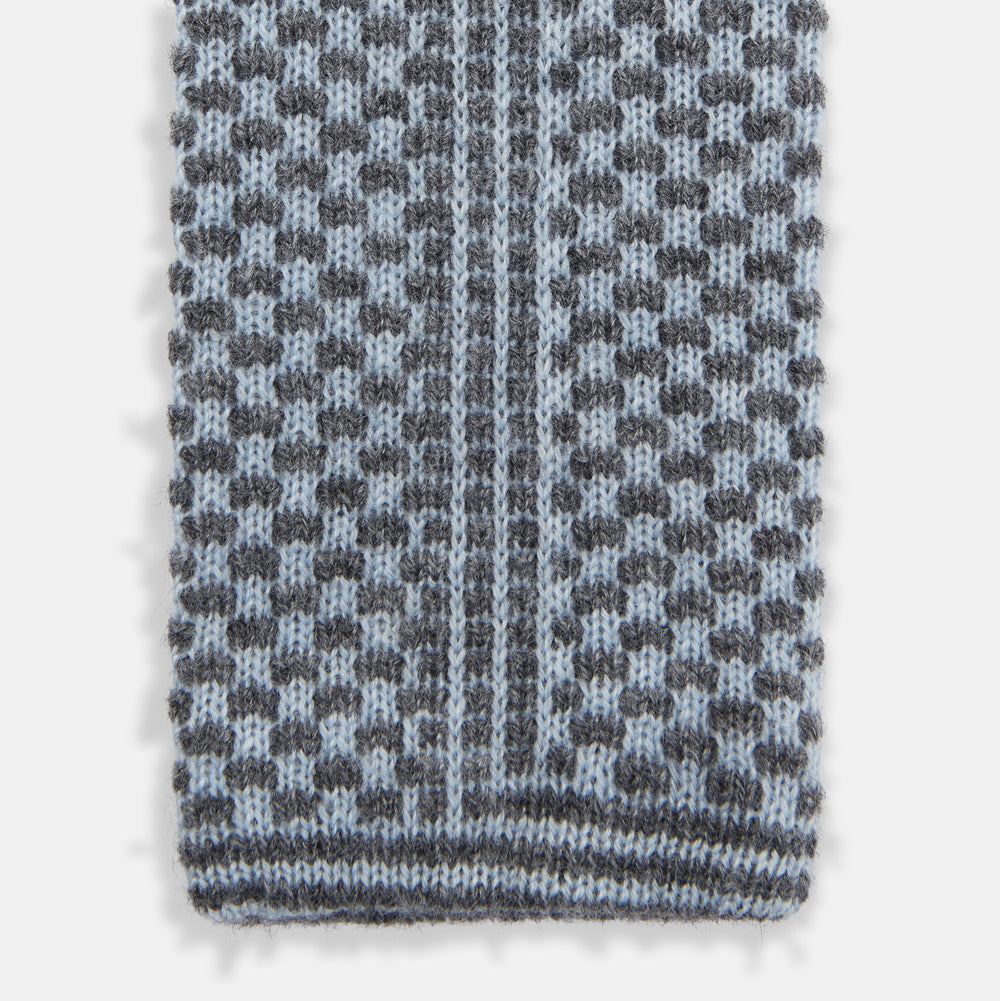 The Turnbull & Asser Pale Blue Multi Cashmere Knitted Tie features a subtle checkered pattern in black and light blue, making it a refined addition to your menswear collection. Shown rolled up on a plain white background.