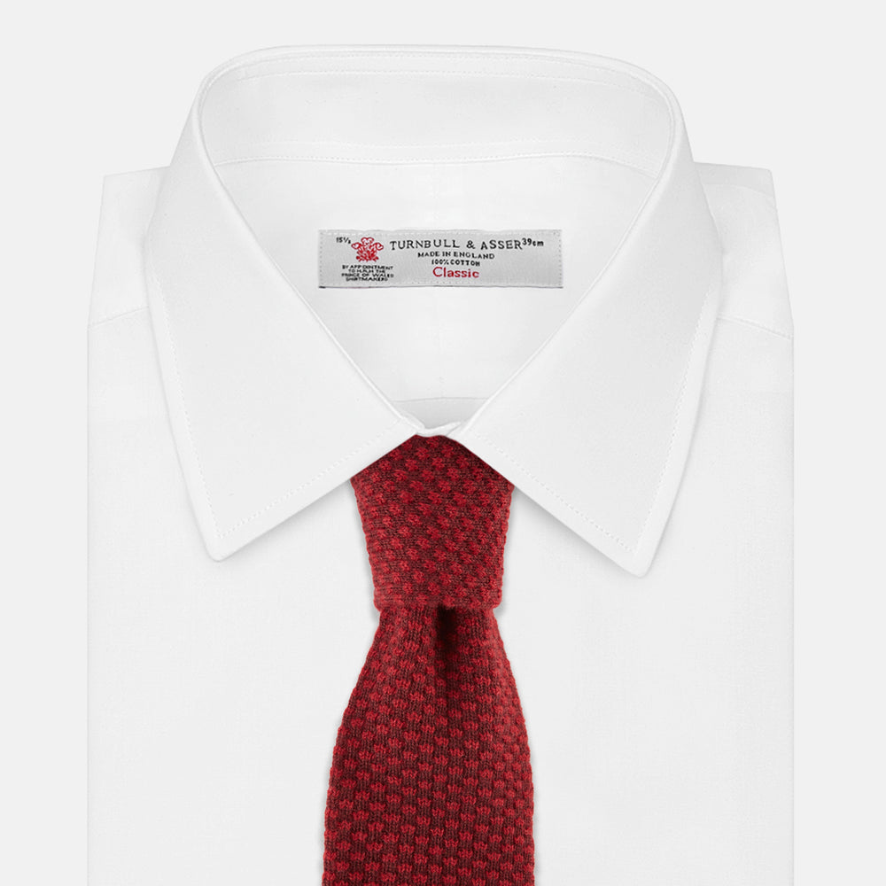 The Turnbull & Asser Red Multi Cashmere Knitted Tie, featuring a textured dark red design, is displayed rolled up on a plain white background.