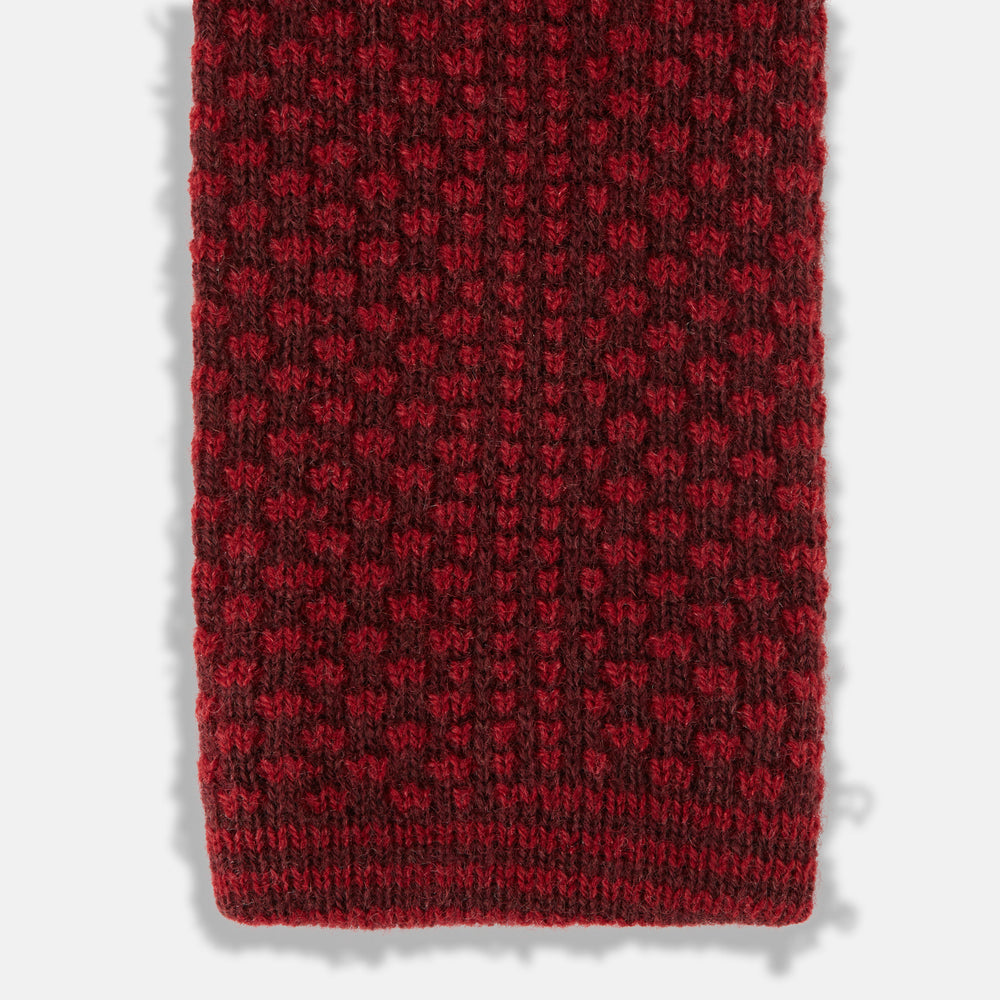 The Turnbull & Asser Red Multi Cashmere Knitted Tie, featuring a textured dark red design, is displayed rolled up on a plain white background.
