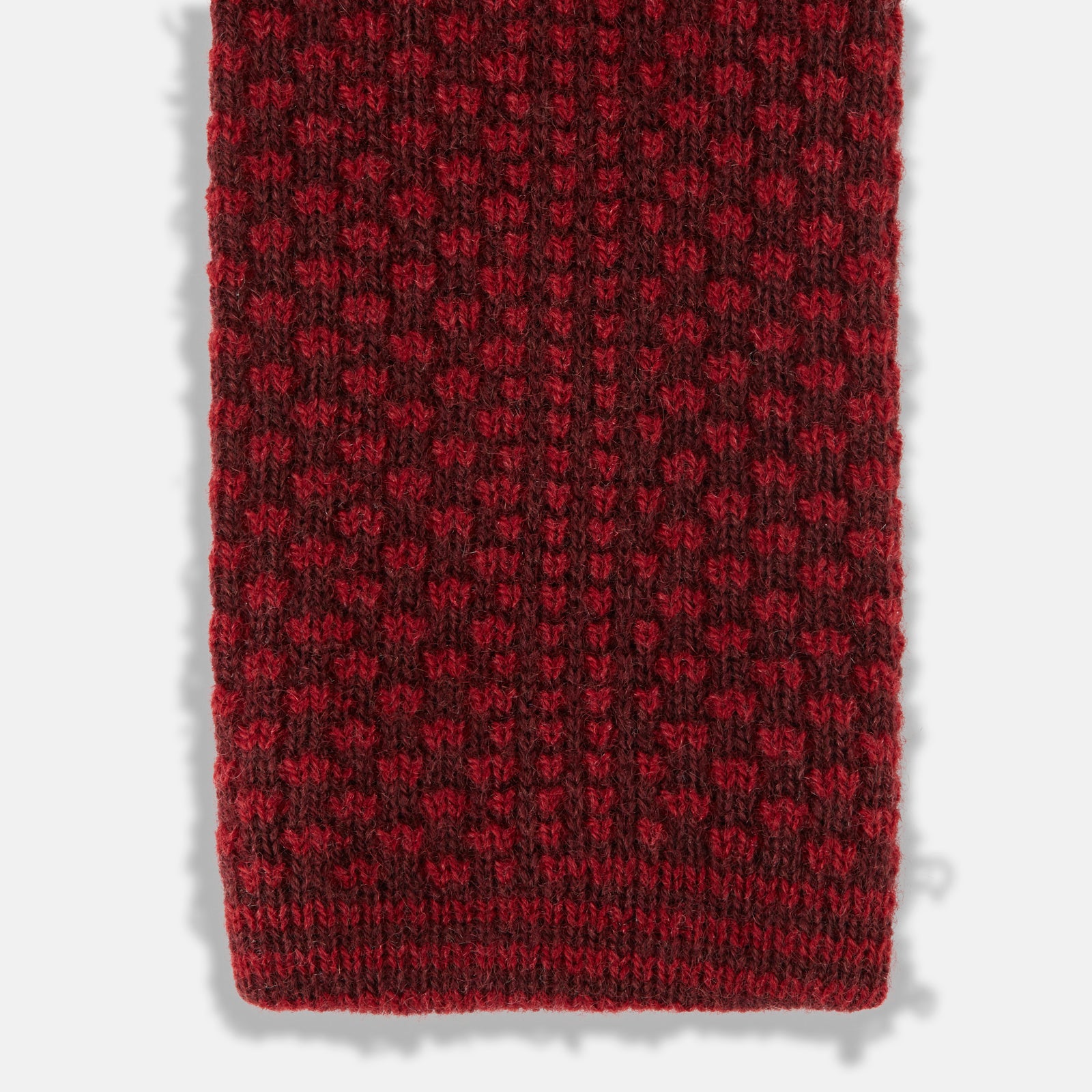 View 4 of product The Turnbull & Asser Red Multi Cashmere Knitted Tie, featuring a textured dark red design, is displayed rolled up on a plain white background.