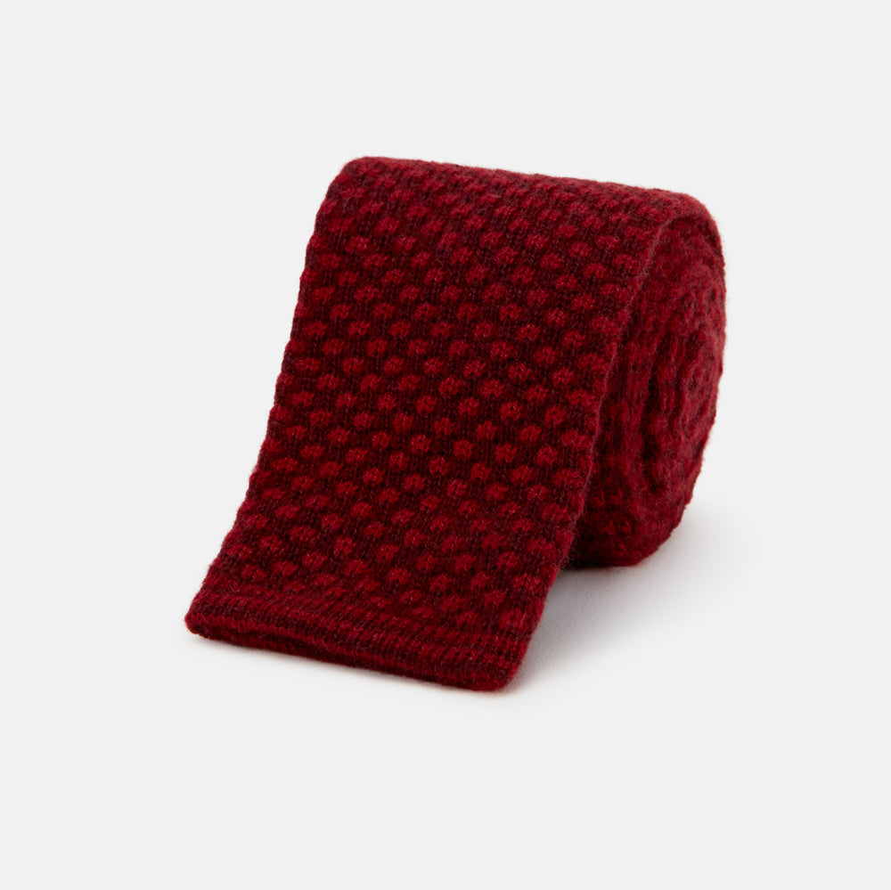 The Turnbull & Asser Red Multi Cashmere Knitted Tie, featuring a textured dark red design, is displayed rolled up on a plain white background.