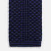 View 4 of product The Turnbull & Asser Navy Multi Cashmere Knitted Tie features a subtle black checkered pattern and is shown rolled up against a plain light background.
