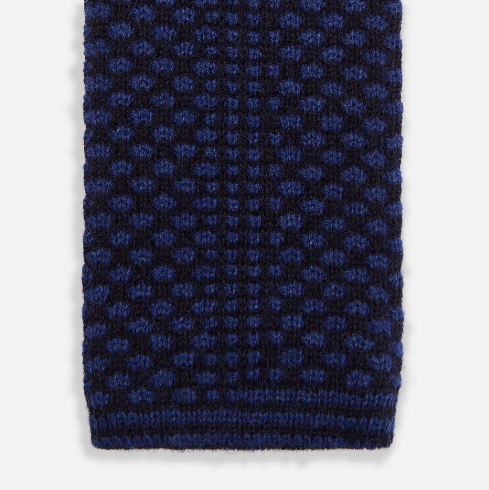 View 4 of product The Turnbull & Asser Navy Multi Cashmere Knitted Tie features a subtle black checkered pattern and is shown rolled up against a plain light background.
