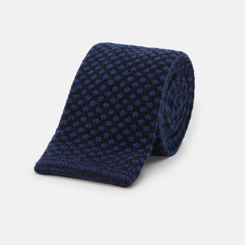 The Turnbull & Asser Navy Multi Cashmere Knitted Tie features a subtle black checkered pattern and is shown rolled up against a plain light background.