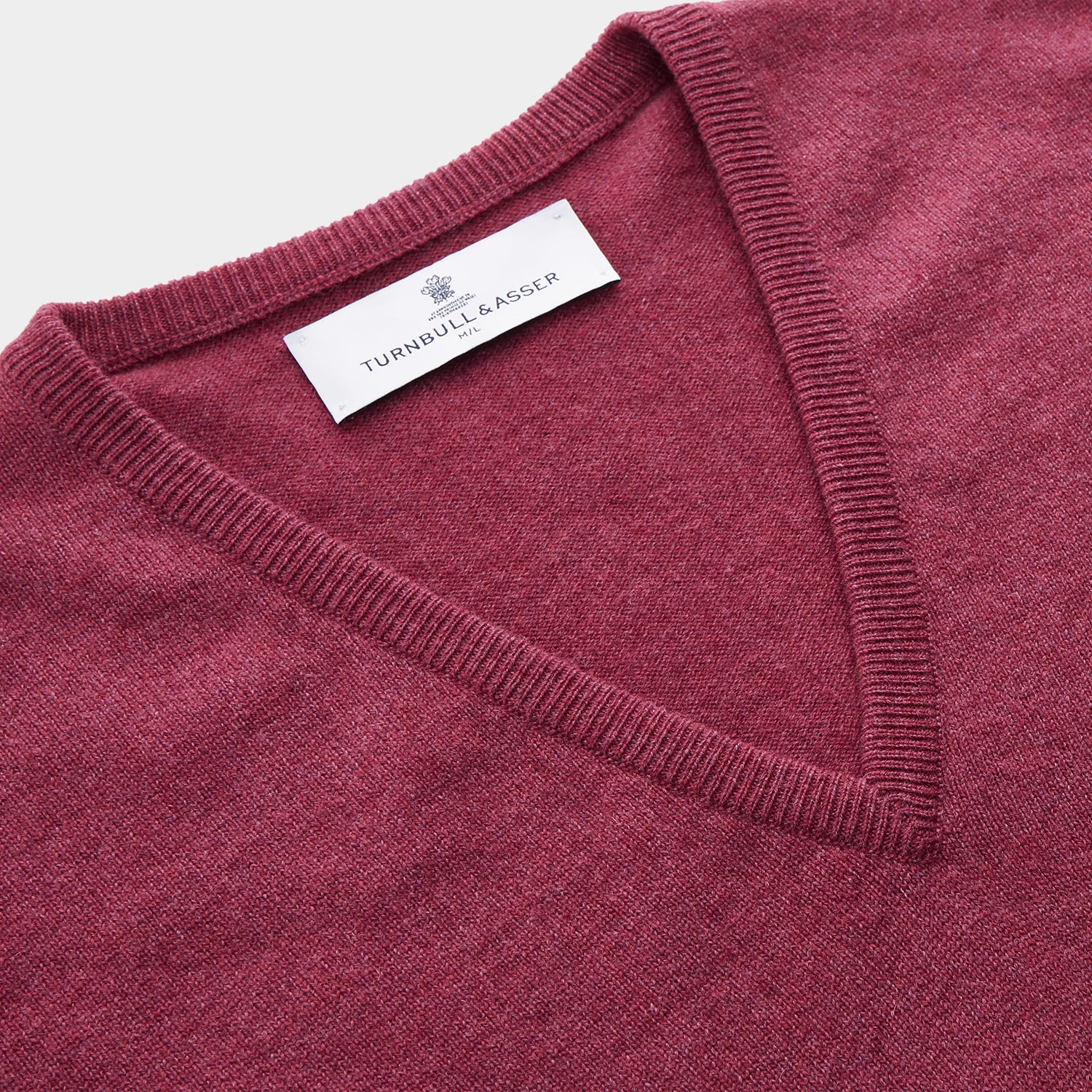 View 2 of product The Turnbull & Asser Soft Burgundy Cashmere V-neck Paden Jumper is displayed flat on a white background, showing off its soft texture and subtle ribbed cuffs and hem.