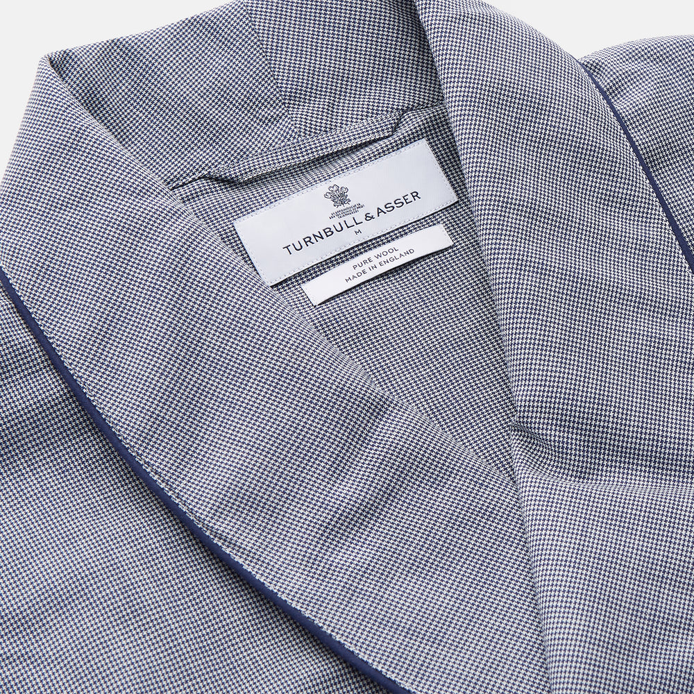 The Navy Houndstooth Wool Arnold Gown by Turnbull & Asser features a shawl collar, front chest pocket, long sleeves, and a matching fabric belt tied at the waist.