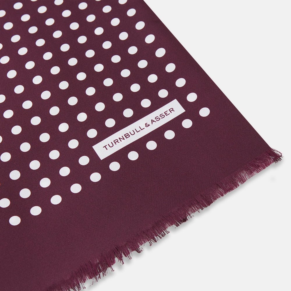 The Turnbull & Asser Purple and White Spotted Silk and Wool Scarf features a deep purple color with white polka dots, frayed edges, and a small white label near one end, shown neatly arranged on a white background.