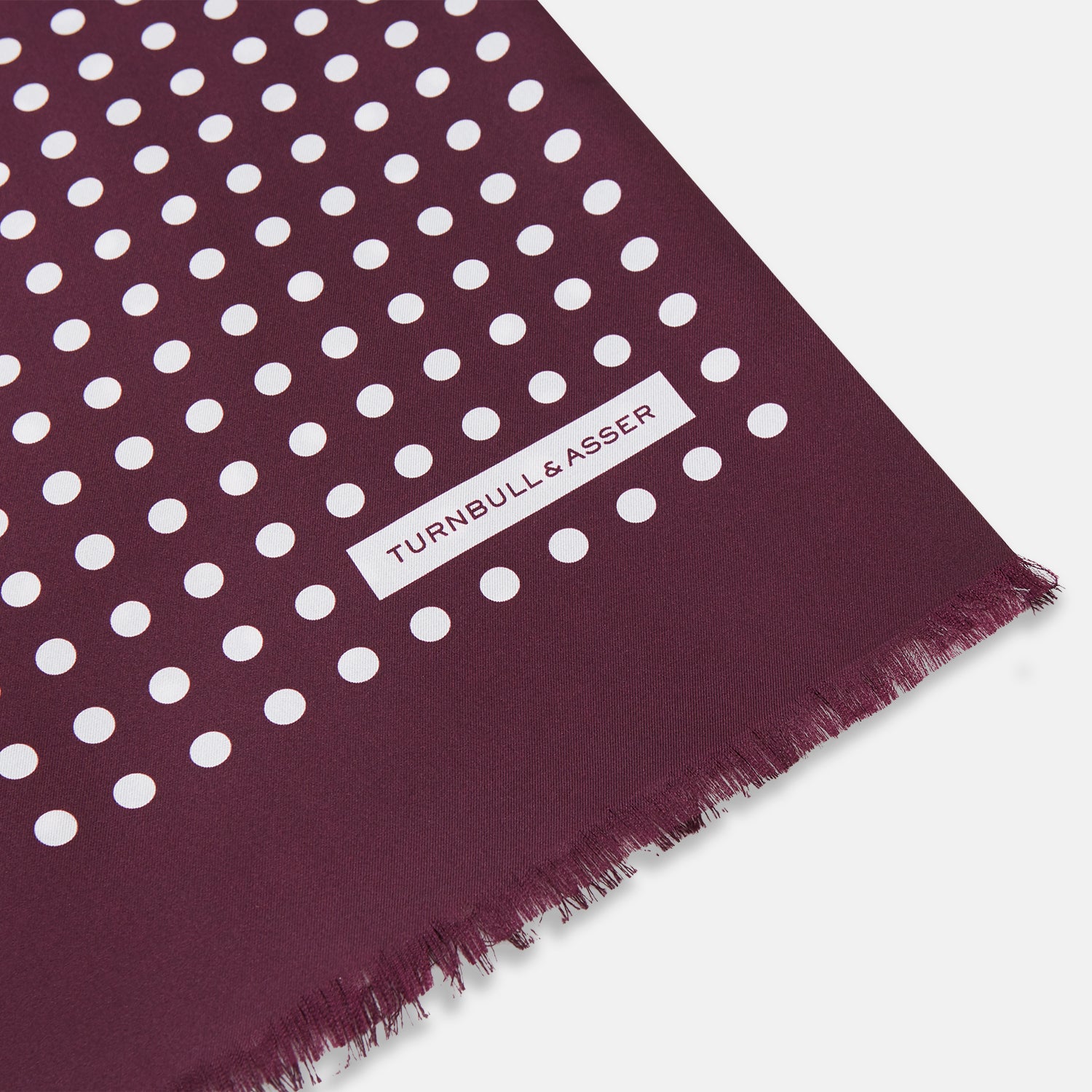 View 2 of product The Turnbull & Asser Purple and White Spotted Silk and Wool Scarf features a deep purple color with white polka dots, frayed edges, and a small white label near one end, shown neatly arranged on a white background.