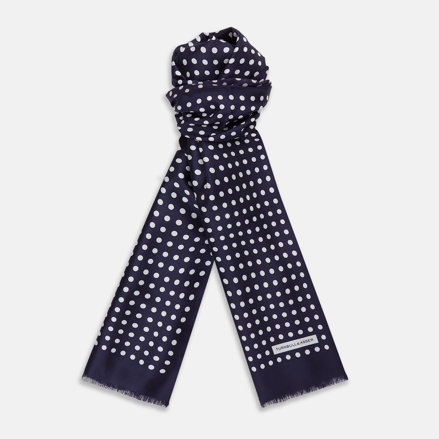 View 1 of product The Turnbull & Asser Navy and Cream Spotted Silk and Wool Scarf features white polka dots, a visible label, slightly frayed edges, and a hand-printed look for unique style.