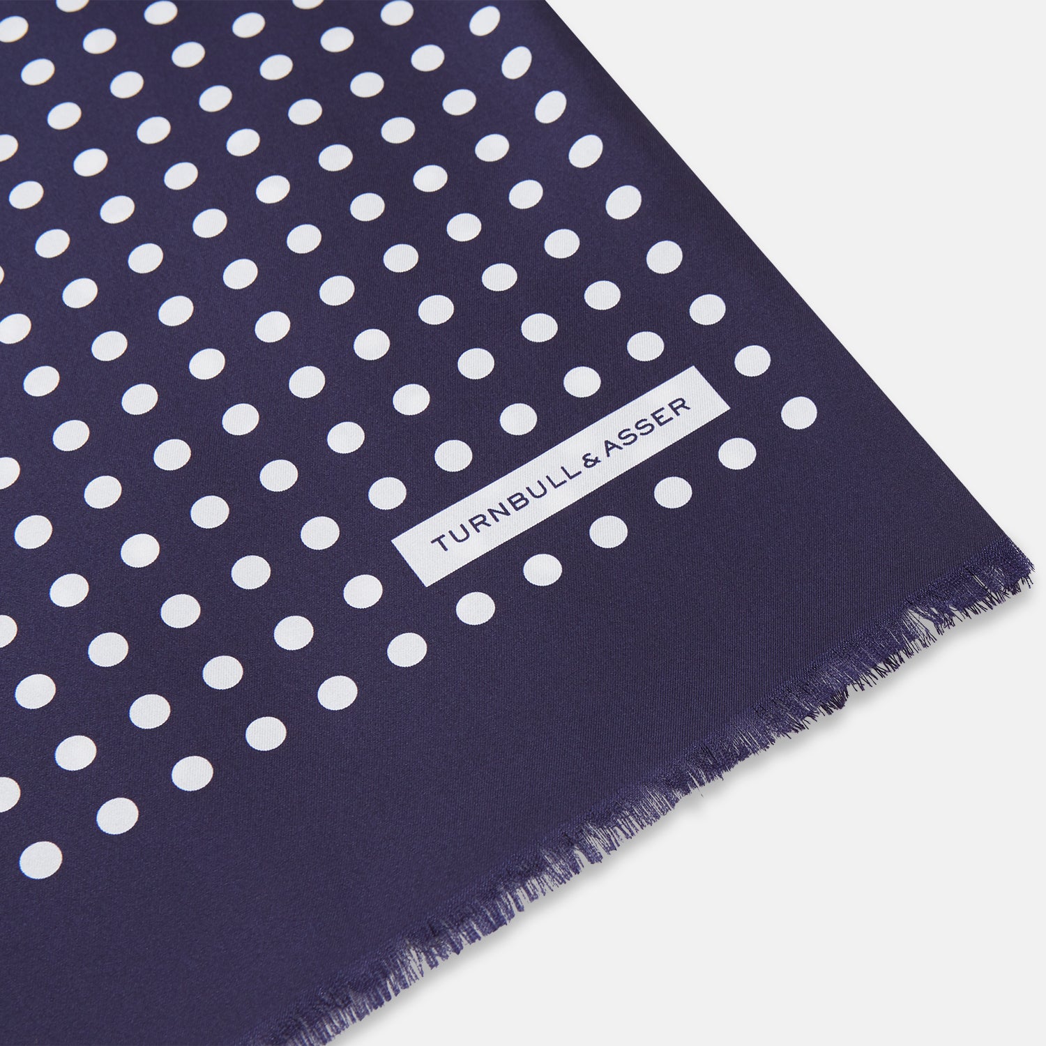 View 2 of product The Turnbull & Asser Navy and Cream Spotted Silk and Wool Scarf features white polka dots, a visible label, slightly frayed edges, and a hand-printed look for unique style.
