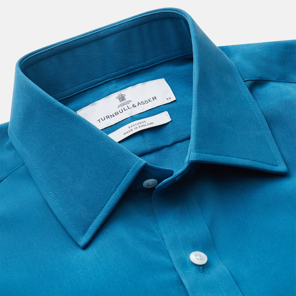 The Turnbull & Asser Blue Silk Regular Fit Mayfair Shirt features long sleeves, a pointed collar, and white buttons in a solid bright blue; displayed flat on a white background.