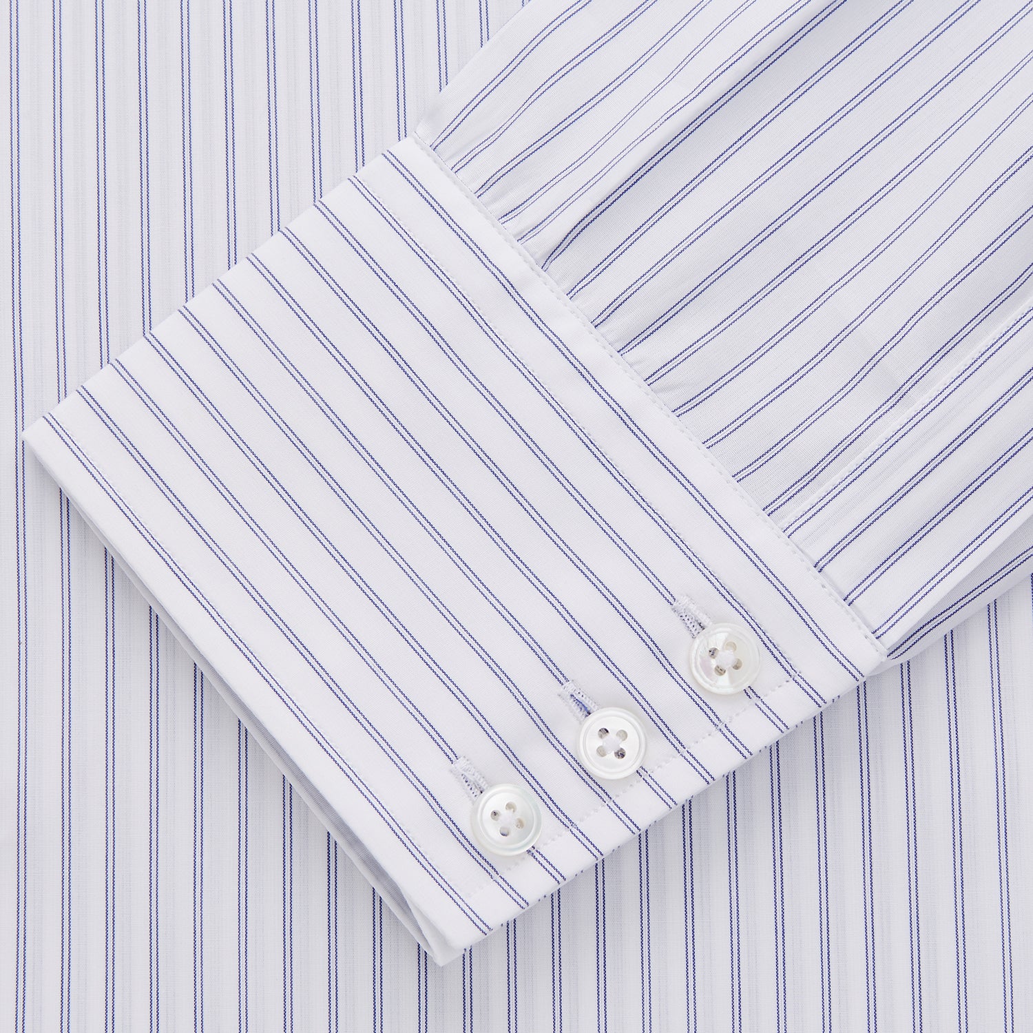 View 2 of product The Turnbull & Asser White and Blue Halo Stripe Cotton Regular Fit Mayfair Shirt features thin vertical stripes, a classic collar, and cuffed long sleeves—an essential men's formal shirt shown laid flat on a white background.