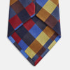 View 3 of product The Turnbull & Asser Blue, Red and Yellow Checker Silk Tie features a bold checkered pattern in red, blue, yellow, brown, and black tones, shown rolled up against a white background.
