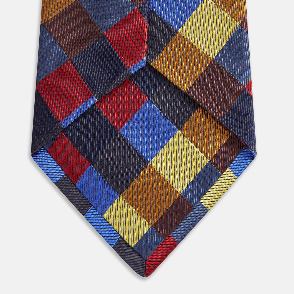 The Turnbull & Asser Blue, Red and Yellow Checker Silk Tie features a bold checkered pattern in red, blue, yellow, brown, and black tones, shown rolled up against a white background.