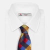 View 4 of product The Turnbull & Asser Blue, Red and Yellow Checker Silk Tie features a bold checkered pattern in red, blue, yellow, brown, and black tones, shown rolled up against a white background.