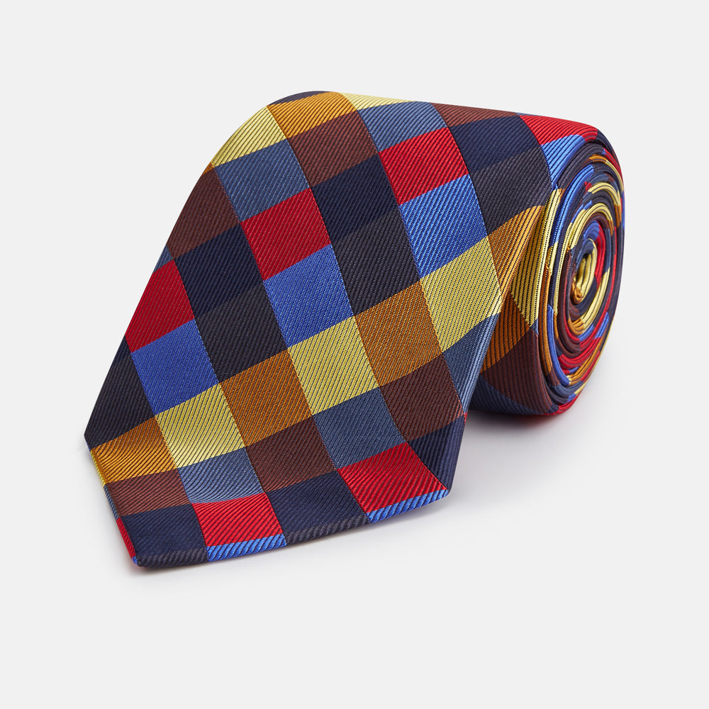 The Turnbull & Asser Blue, Red and Yellow Checker Silk Tie features a bold checkered pattern in red, blue, yellow, brown, and black tones, shown rolled up against a white background.