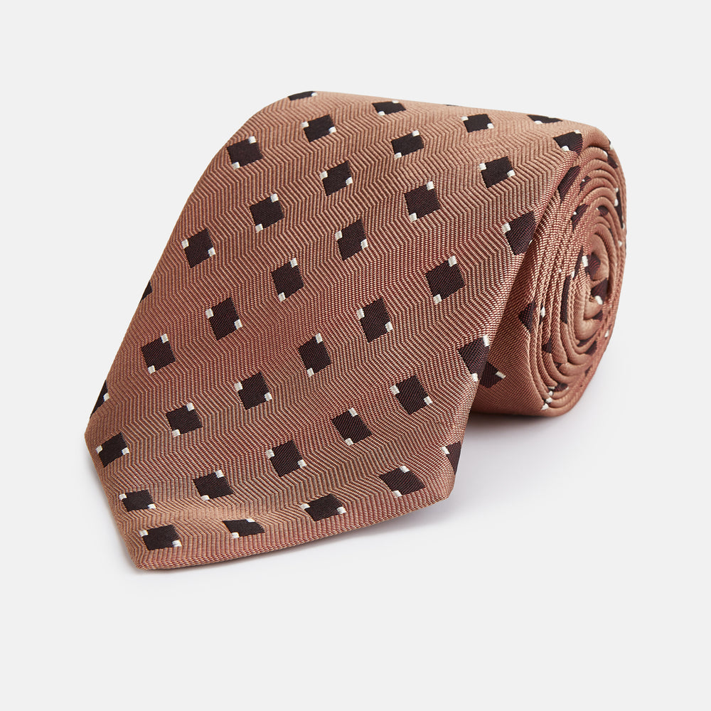 The Bronze and Chocolate Brown Tile Silk Tie by Turnbull & Asser features a classic tile pattern with small black graduation caps, neatly rolled on a plain white background.