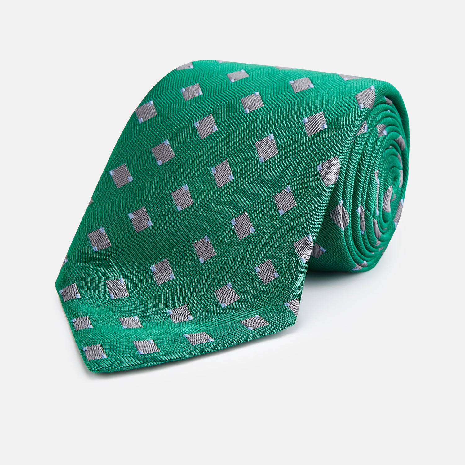 View 1 of product The Turnbull & Asser Kelly Green and Grey Tile Silk Tie features a subtle chevron texture and classic grey tile pattern, displayed rolled on a white background.