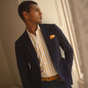 View 3 of product A man stands against a tan background wearing a Turnbull & Asser Orange Multi Stripe Regular Fit Shirt with T&A Collar and 3 Button Cuffs, paired with tan dress pants, brown belt, and brown shoes. He faces forward with a neutral expression.