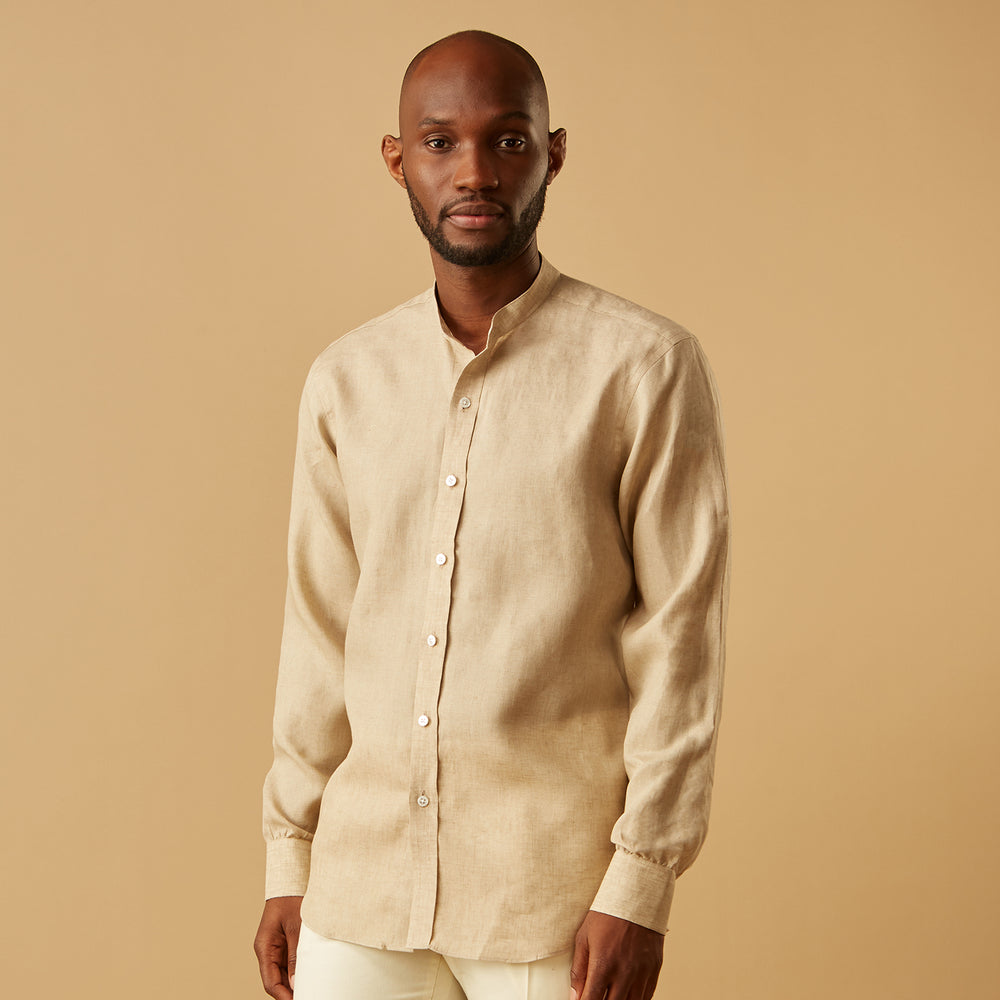 A man with a bald head and trimmed beard wears the Turnbull & Asser Beige Weekend Fit Linen Blake Shirt with stand collar and 1-button cuffs, standing calmly against a matching beige background.