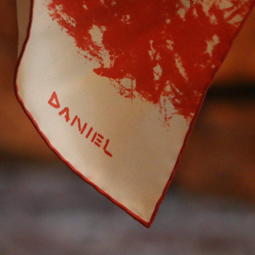 The Turnbull & Asser DANIEL PERKIN BLUE WILDCAT POCKET SQUARE features a blue-toned sketch of a tabby cat’s face with vivid eyes and fine fur detail on a pale blue background, finished with “DANISL” in the lower right corner.
