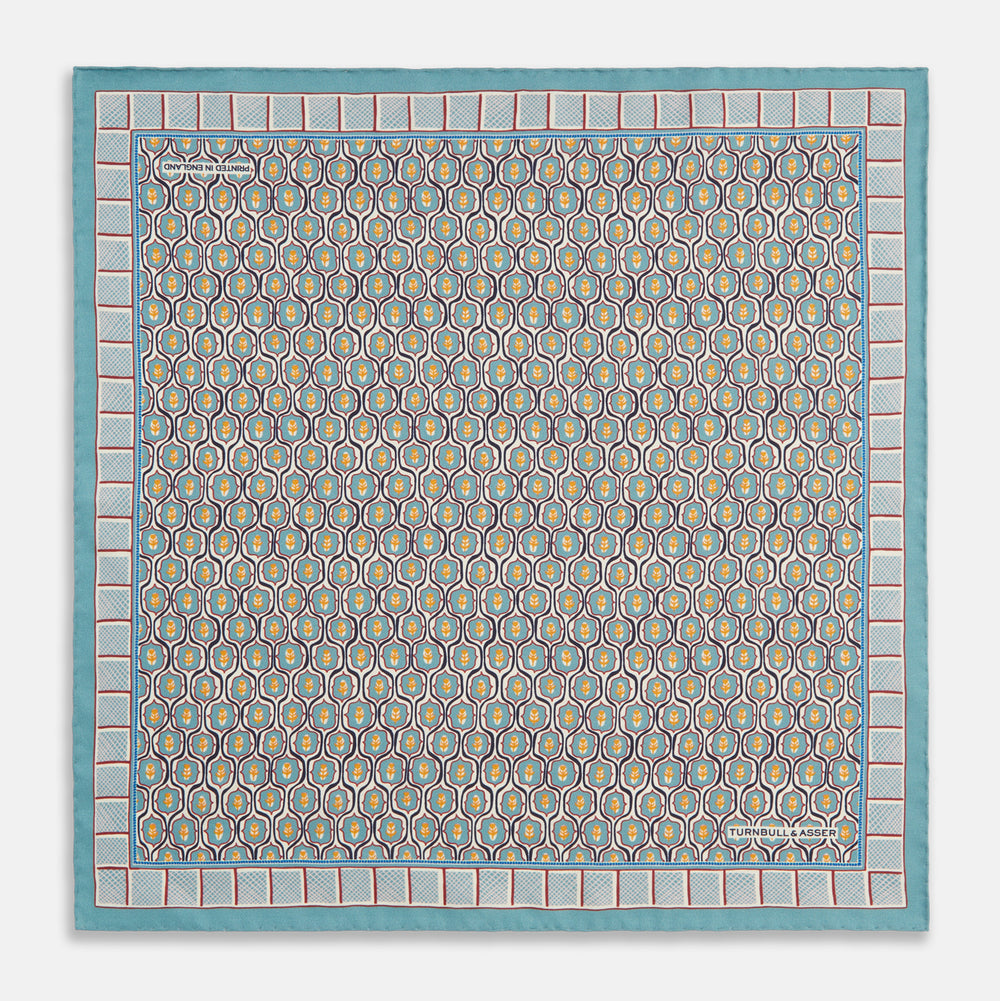 The Turquoise Flower Bloomsbury-Inspired Pattern Silk Pocket Square by Turnbull & Asser features a vibrant geometric floral motif with a turquoise border for a colorful, symmetrical accent.