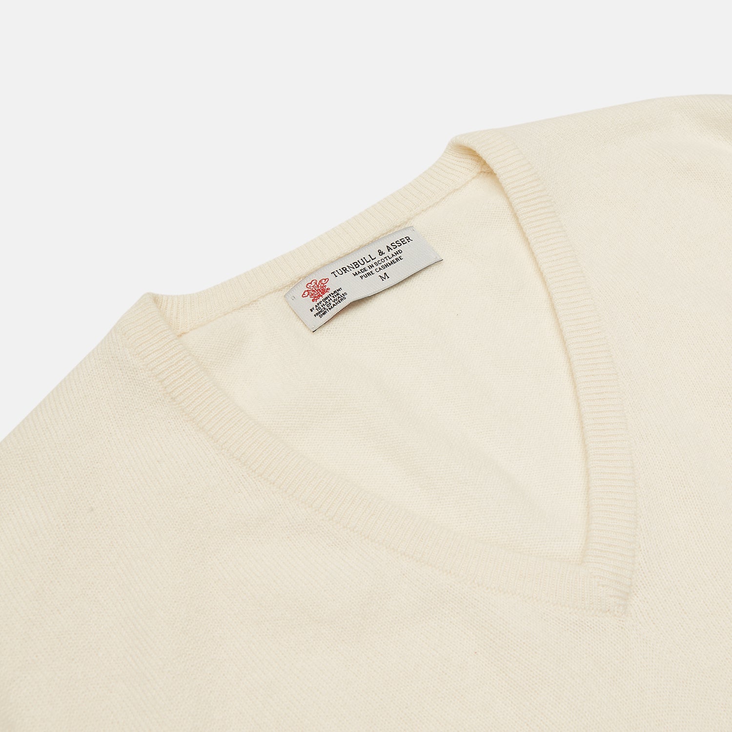 View 2 of product The Turnbull & Asser Cream Cashmere V-Neck Jumper is a luxury knitwear piece with ribbed cuffs and hem, shown laid flat on a white background. Its classic long-sleeve style offers timeless elegance.