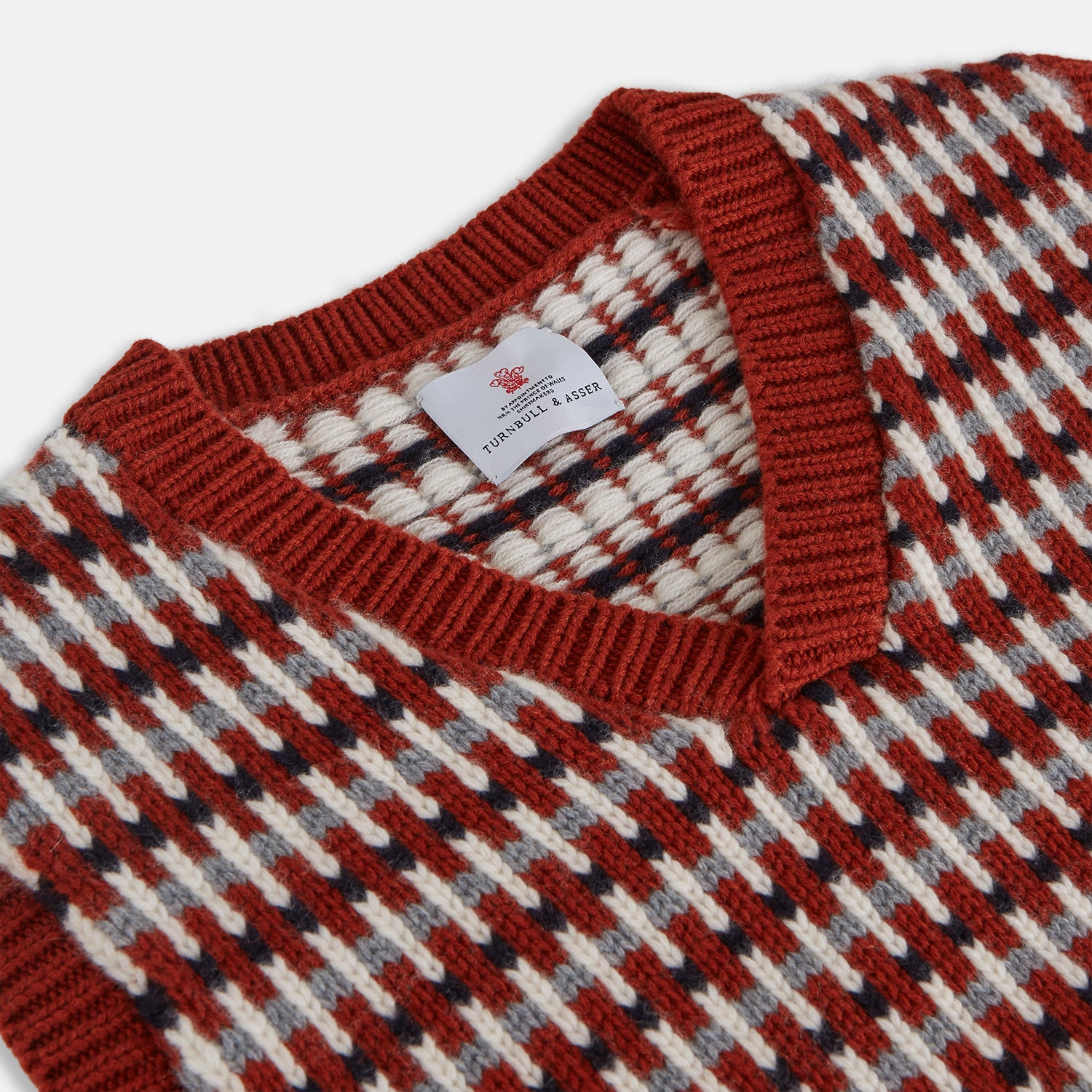View 4 of product The Rust Knitted Cashmere Slipover by Turnbull & Asser is a sleeveless V-neck vest in red, white, and dark brown houndstooth, inspired by Welsh knitwear with solid red ribbed trim at the collar, armholes, and hem.