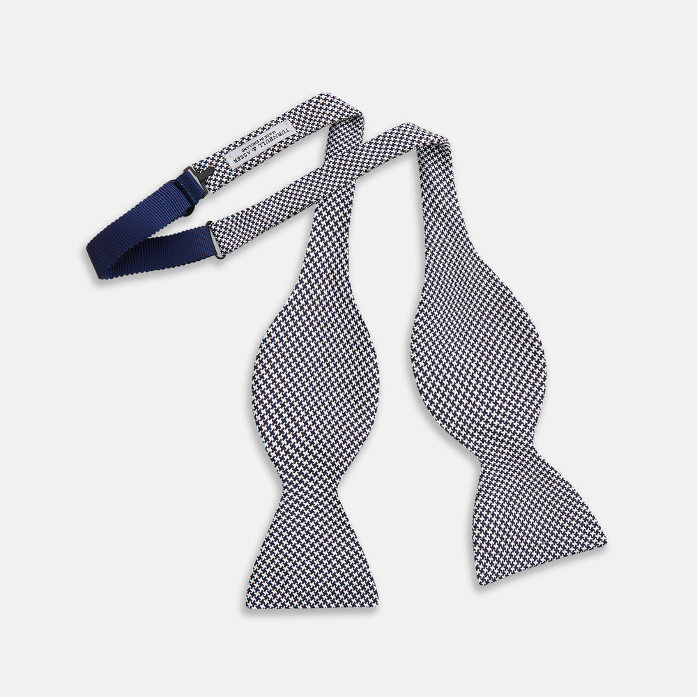 The Turnbull & Asser Black Houndstooth Silk Bow Tie features a classic black and white pattern, displayed against a plain white background—an elegant choice to elevate any formal ensemble.