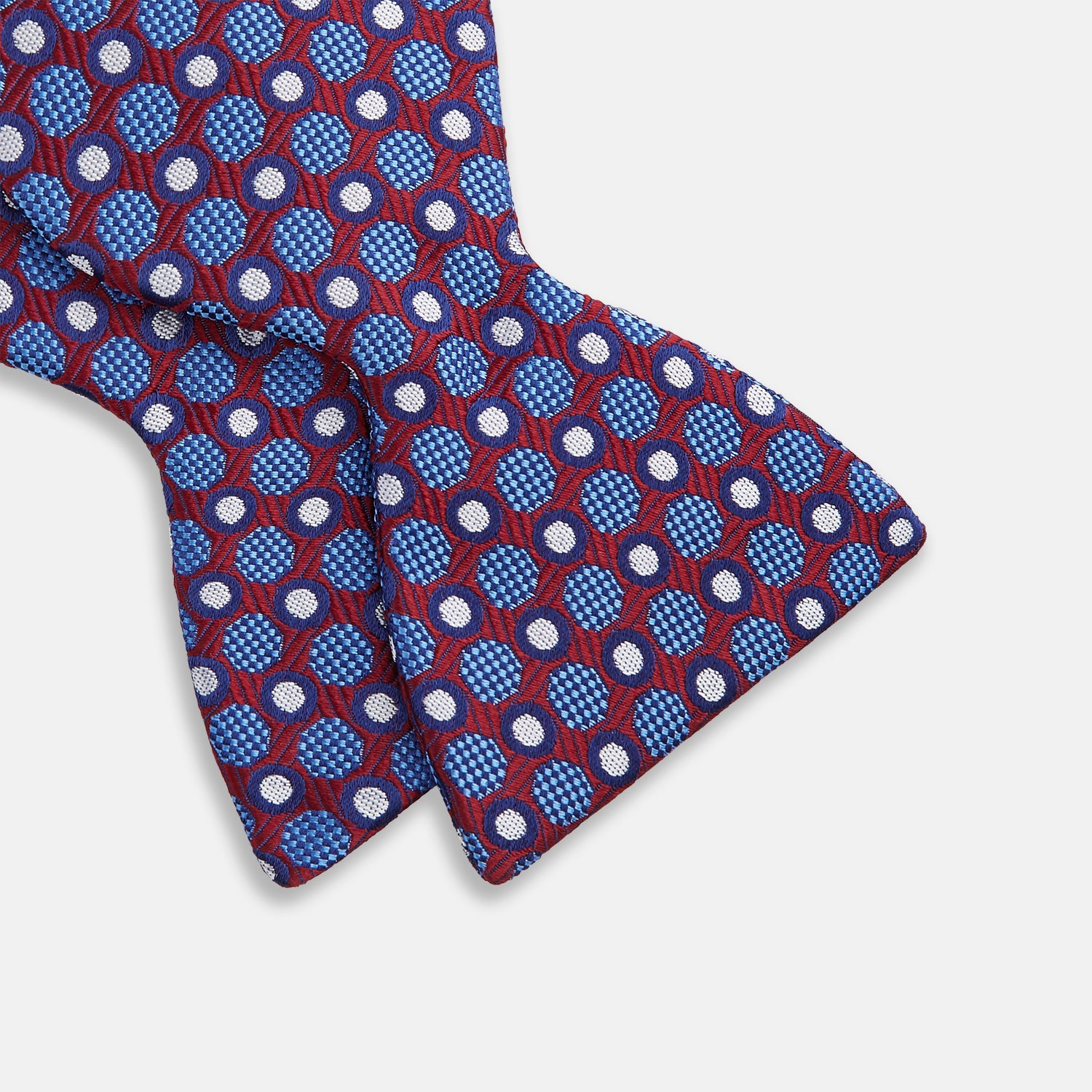 View 3 of product The Turnbull & Asser Burgundy and Blue Circle and Spot Silk Bow Tie showcases a formal patterned design of circles and spots on silk, presented on a plain white backdrop.