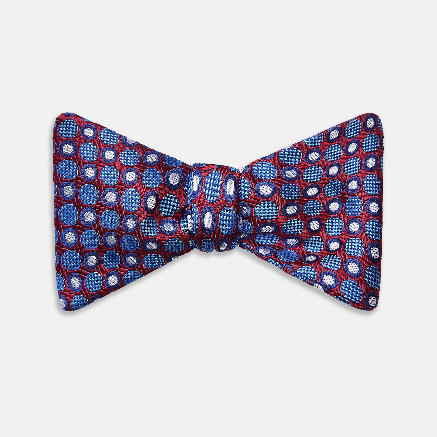 View 1 of product The Turnbull & Asser Burgundy and Blue Circle and Spot Silk Bow Tie showcases a formal patterned design of circles and spots on silk, presented on a plain white backdrop.