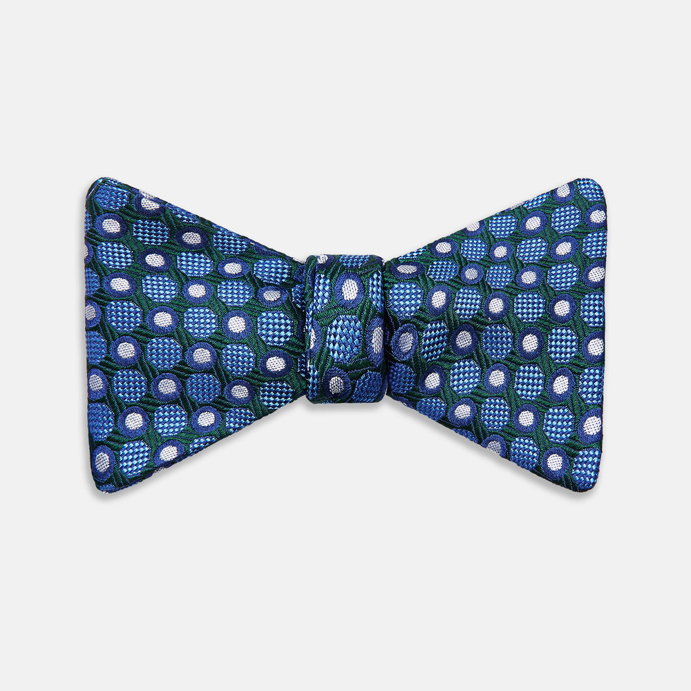 The Turnbull & Asser Forest Green and Blue Circle and Spot Silk Bow Tie showcases a blue, green, and white dotted pattern, set against a plain white background.