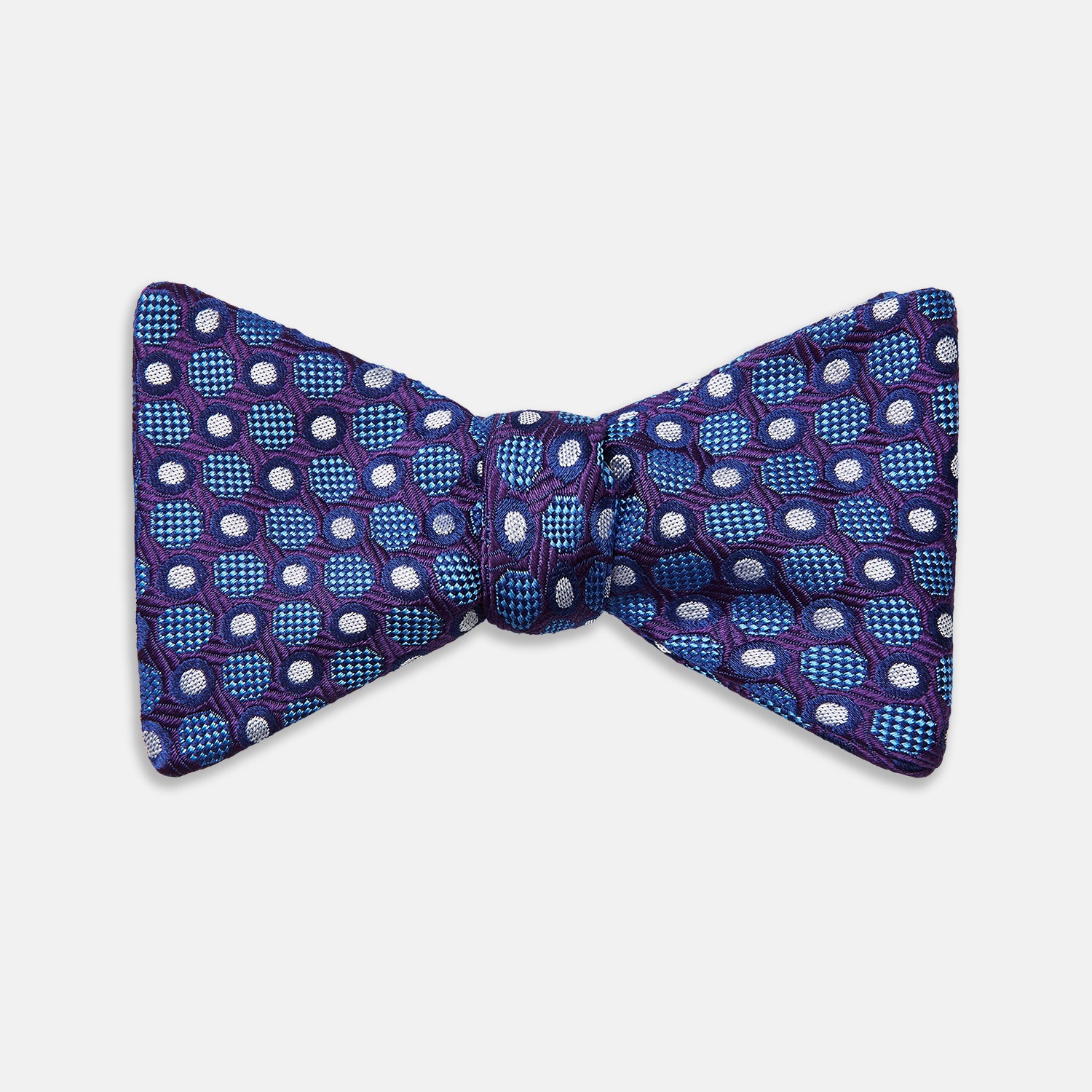 View 1 of product The Turnbull & Asser Plum and Blue Circle and Spot Silk Bow Tie, featuring blue with white and light blue dots on a purple background, is displayed on a plain white surface.