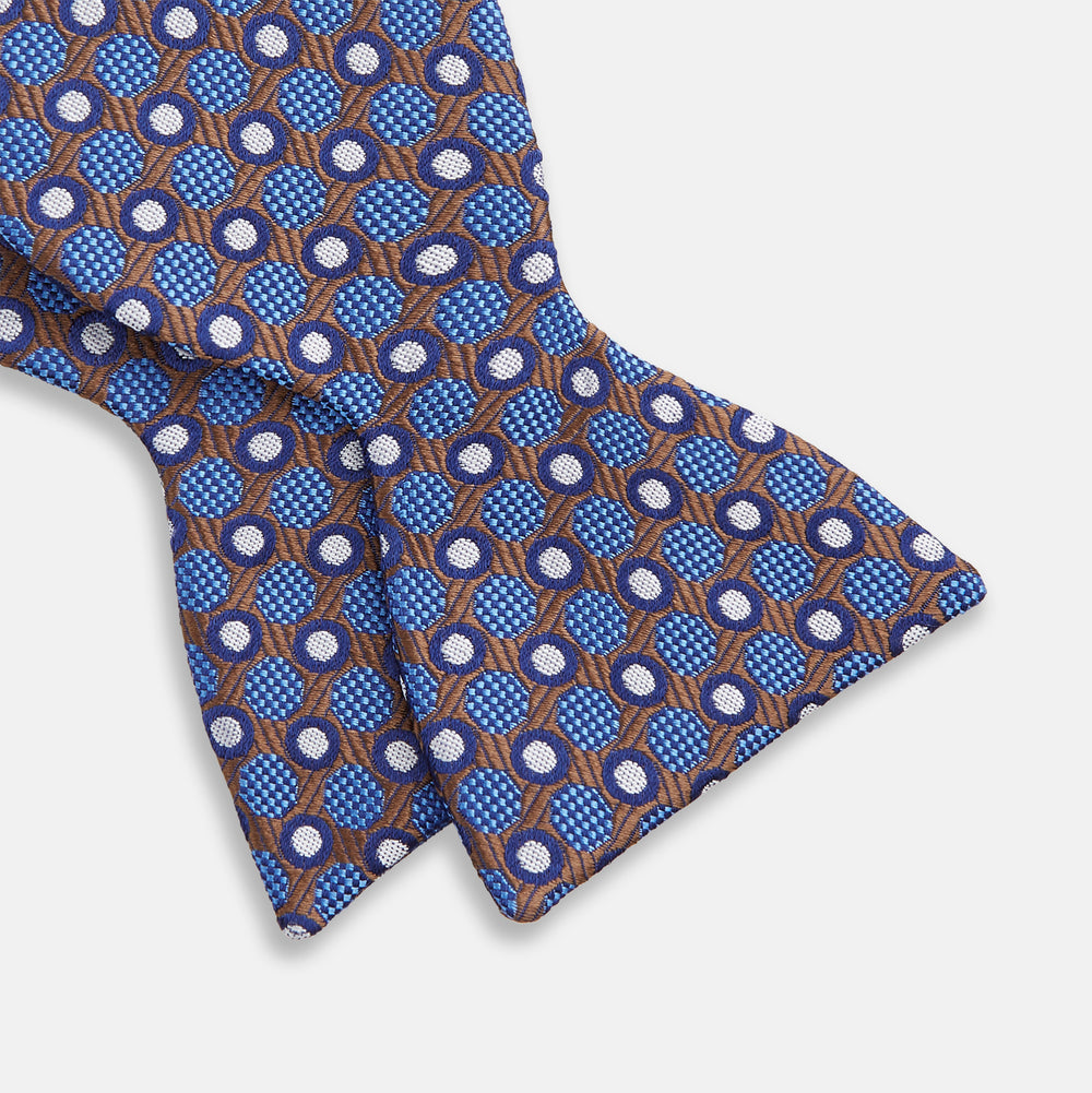 The Turnbull & Asser Brown and Blue Circle and Spot Silk Bow Tie features a blue silk base with light blue and brown circular dots on textured fabric, shown against a white background.